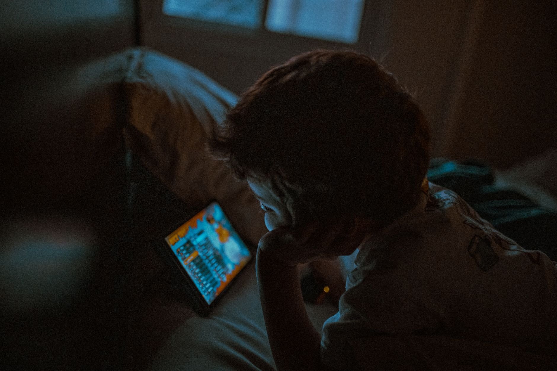 A young child is intently watching a tablet in a cozy, dimly lit room, creating a serene nighttime ambiance.